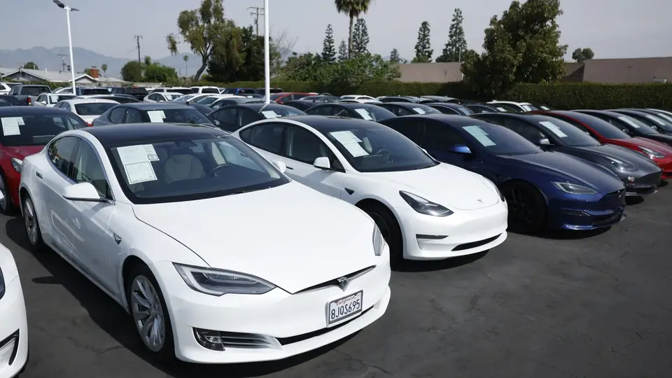 Rows of newly manufactured Tesla vehicles sit in a distribution lot awaiting delivery.