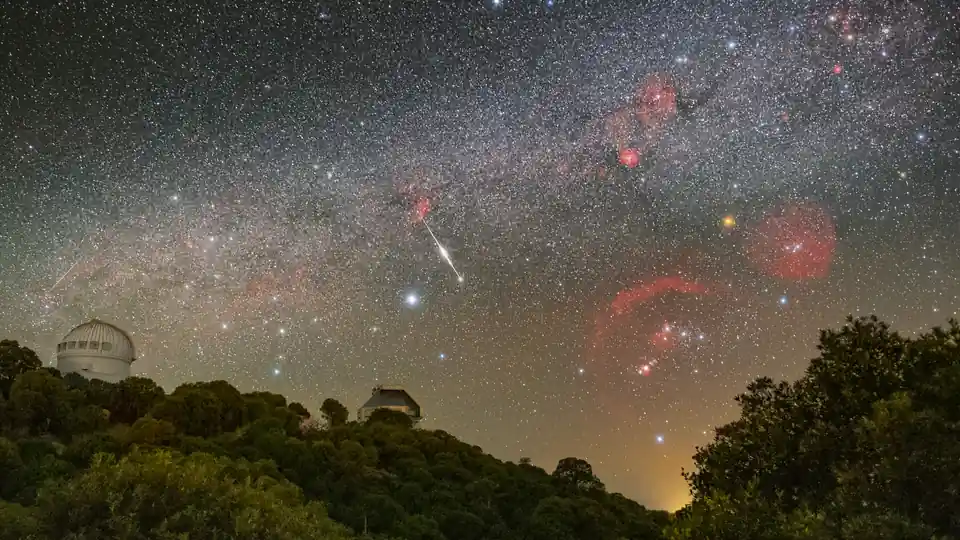 Astronomical observatories under a star-filled sky capturing a brilliant meteor streak during an outburst.